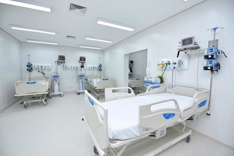 #PraCegoVer: Há três camas hospitalares na imagem. Elas estão em uma sala. A sala é clara, as paredes e o chão são da cor branca. 