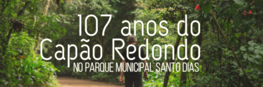 Fotografia de um senhor caminhando em uma "trilha" em meio à vegetação do Parque Santo Dias. Sobre a imagem, estão aplicados os seguintes dizeres ao centro: "107 anos do Capão Redondo no Parque Santo Dias".