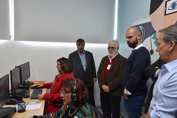 #PraCegoVer: prefeito Bruno Covas e secretário de saúde Edson Aparecido, com outros representantes da plataforma Telemedicina. Na foto, há ainda funcionárias sentadas utilizando a plataforma no computador. 