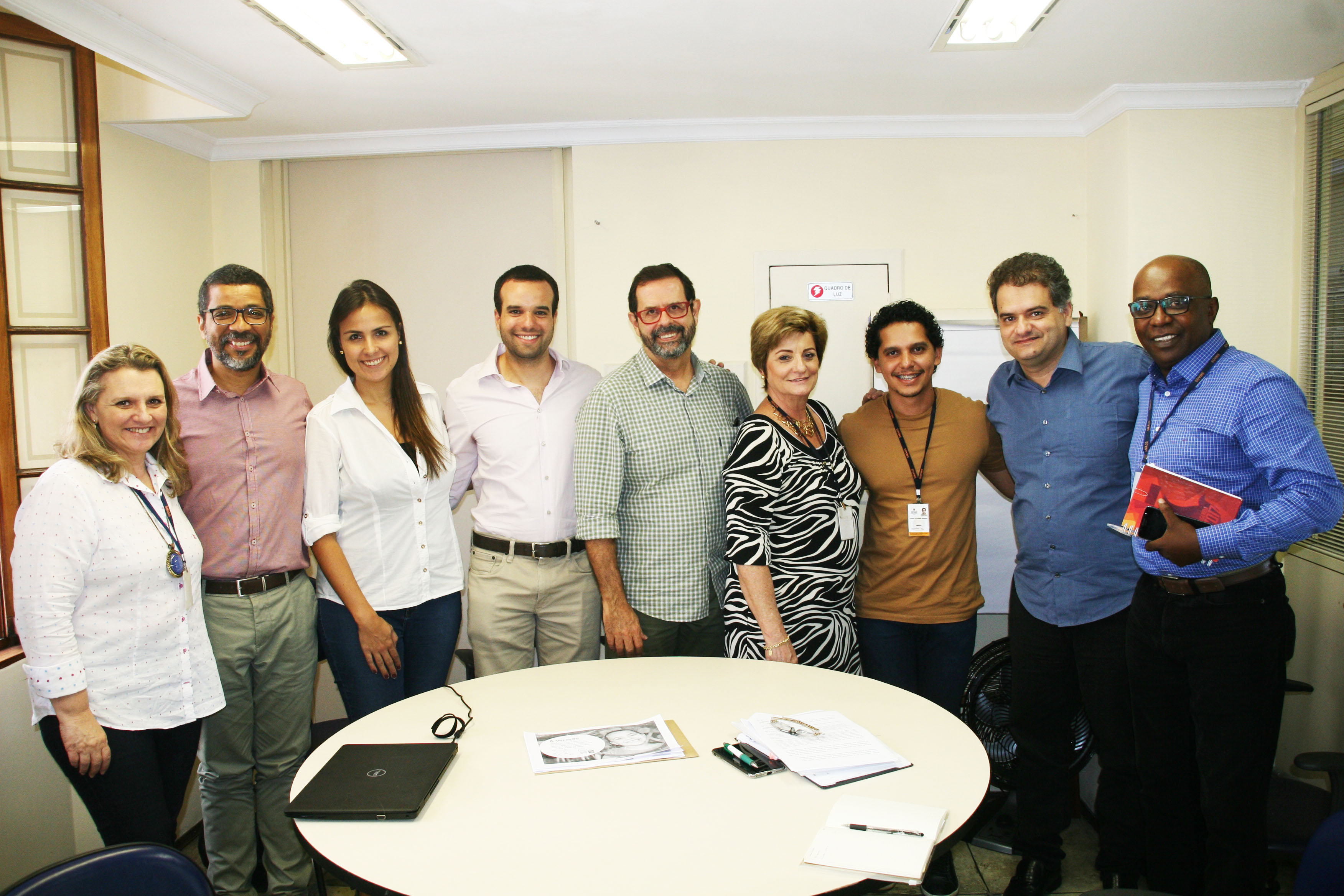 Secretário de SMADS, Marcelo Del Bosco, juntamente com oito servidores públicos em sala com mesa redonda ao centro e todos em pé atrás dela sorrindo para foto