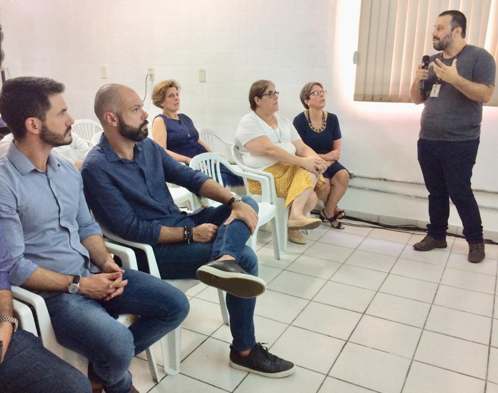 Gerente de Gestão de Benefícios da SMADS se apresenta em pé para plateia com prefeito e secretário da SMADS, entre outros
