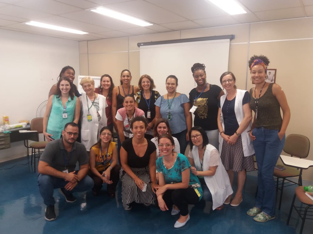 Dezessete pessoas em pose para foto, sete delas agachadas a frente e dez em pé na parte de trás em sala com painel de projeção ao fundo