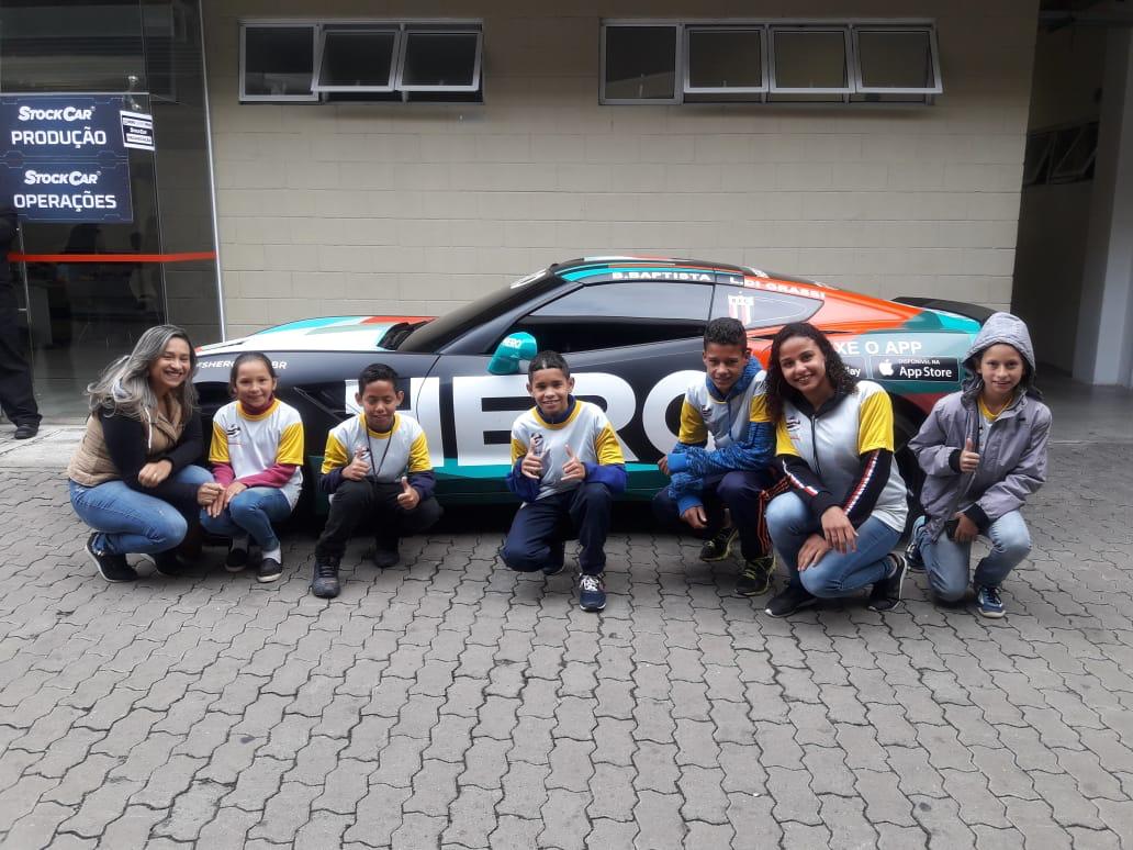 Crianças e instrutores agachados na frente de um carro de corrida