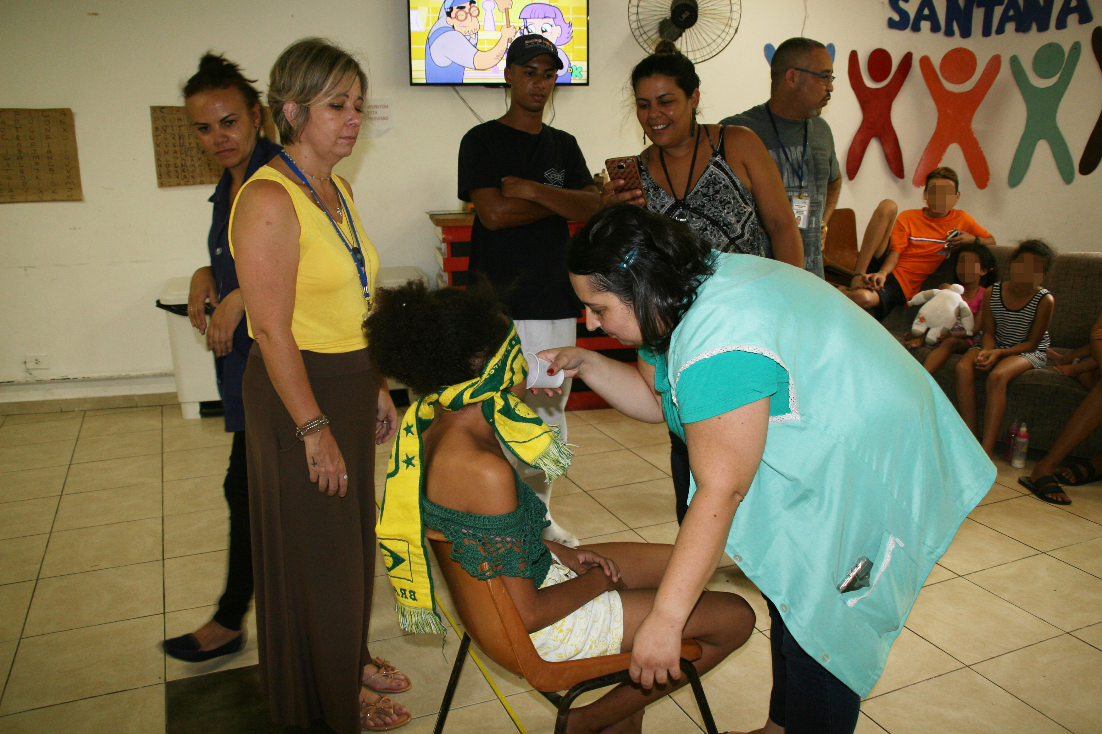Criança usuária do serviço participa de jogo vendada, sentada em cadeira com outros participantes em volta  