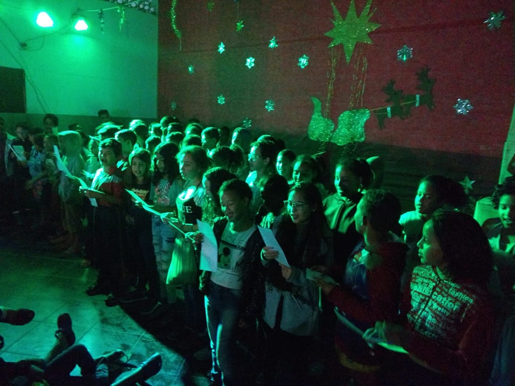 Crianças cantam juntas na cantata de Natal em ambiente de luz verde 