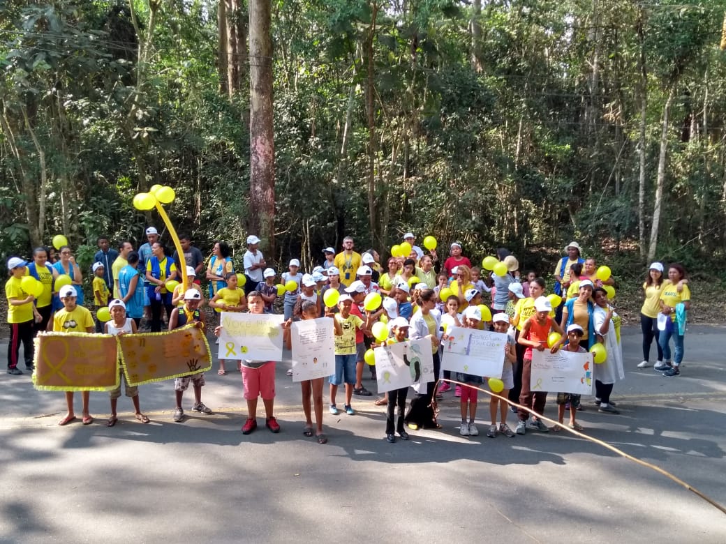 Aproximadamente 140 pessoas, com peças de roupas e bexigas na cor amarela, exibindo faixas e cartazes com frases de valorização à vida. 