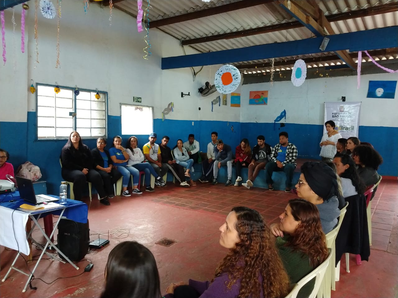 Dezenas de pessoas estão dentro de uma sala de aula, reunidas para a foto.