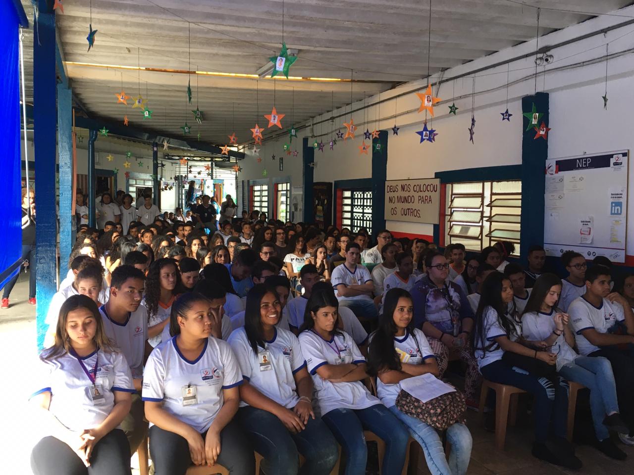 Pátio onde estão aproximadamente 280 pessoas, em sua maioria sentadas, assistindo a apresentações. 