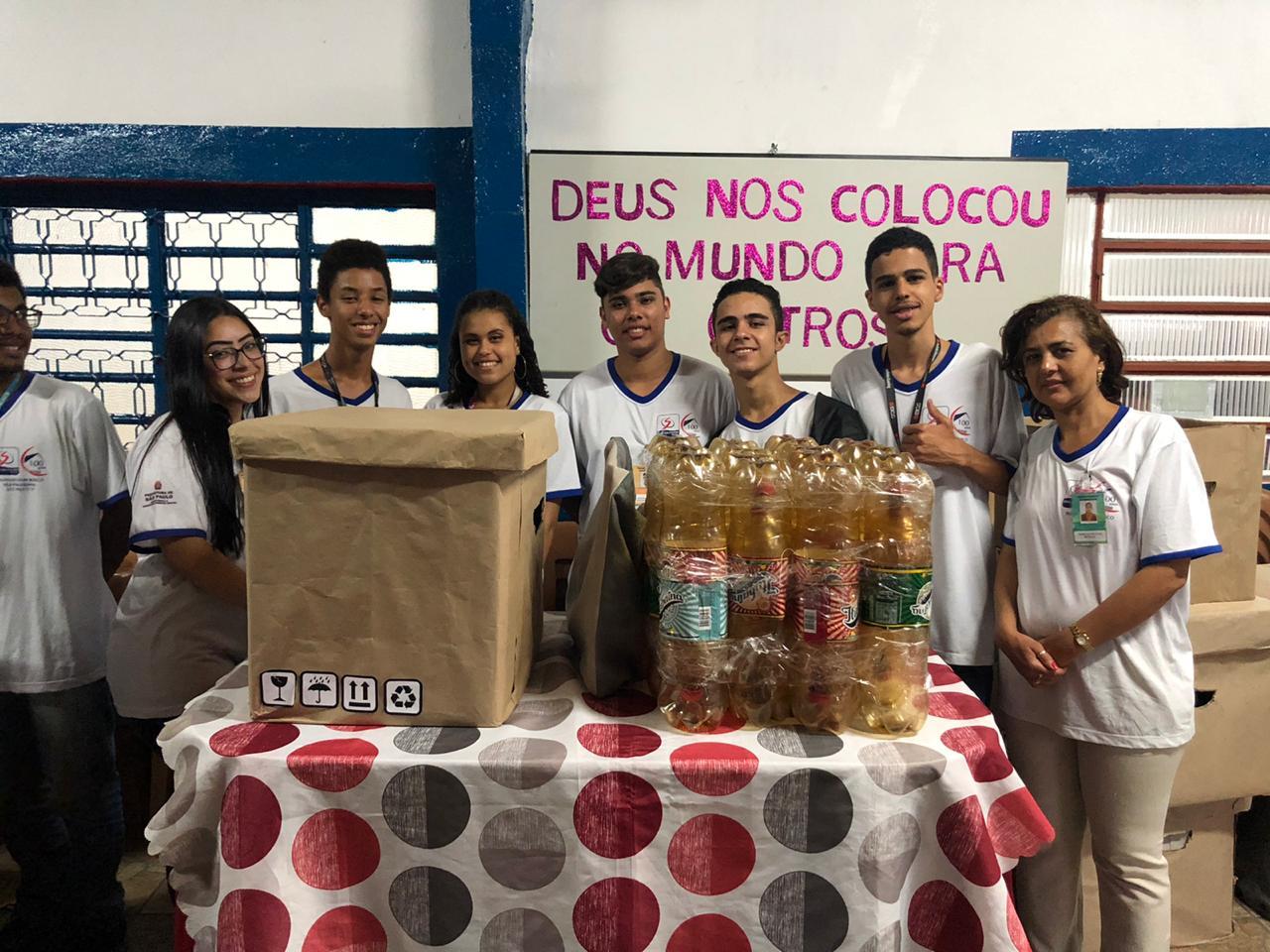 Sete alunos sorrindo para a foto, atrás de mesa que expõe projeto educacional desenvolvido pelos mesmos. 