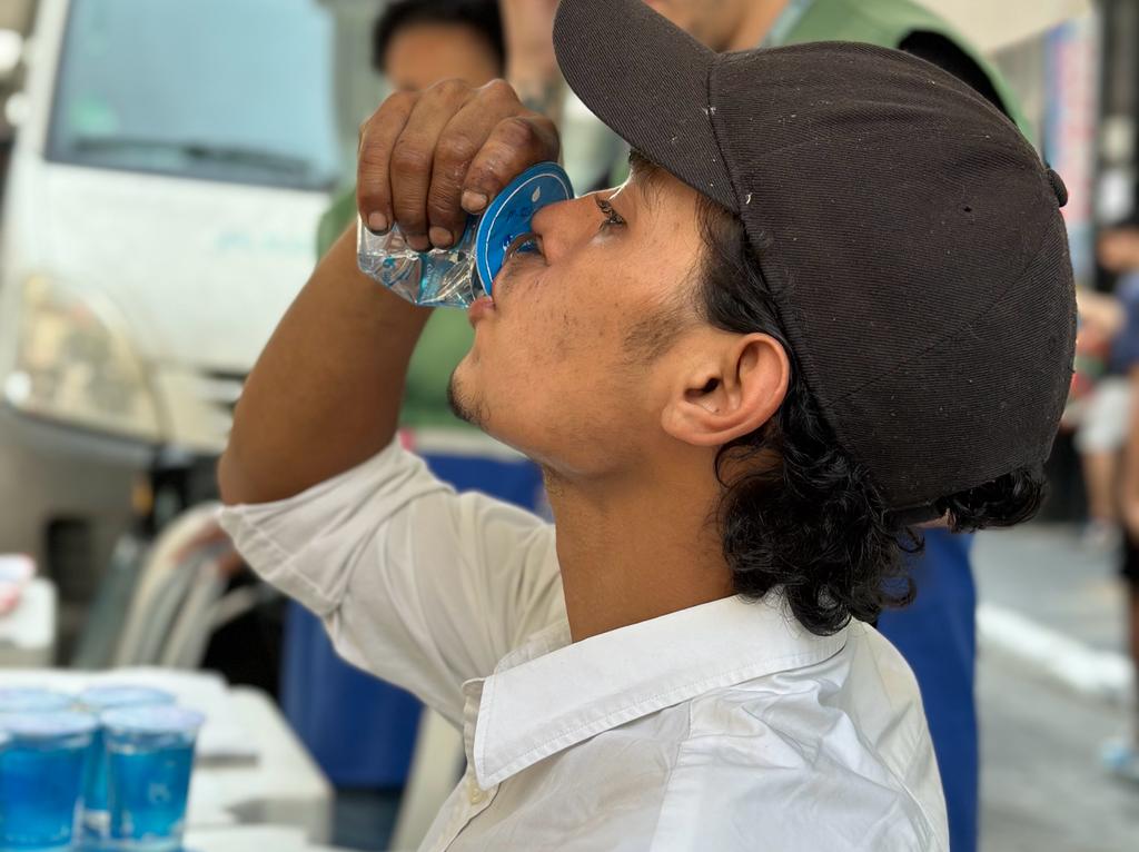 Foto de um homem tomando água em um copo de plástico durante o atendimento em uma das tendas da Operação Altas Temperaturas.