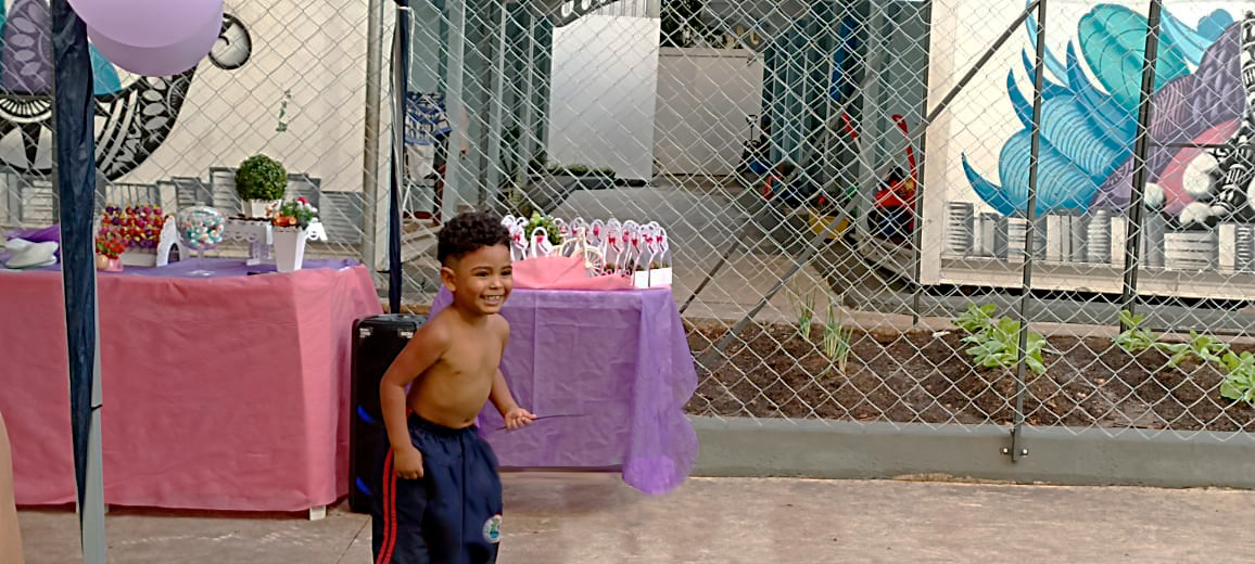Imagem de uma criança correndo pela Vila Reencontro Anhangabaú. Ao fundo, a decoração do aniversário em cima de mesas coloridas.