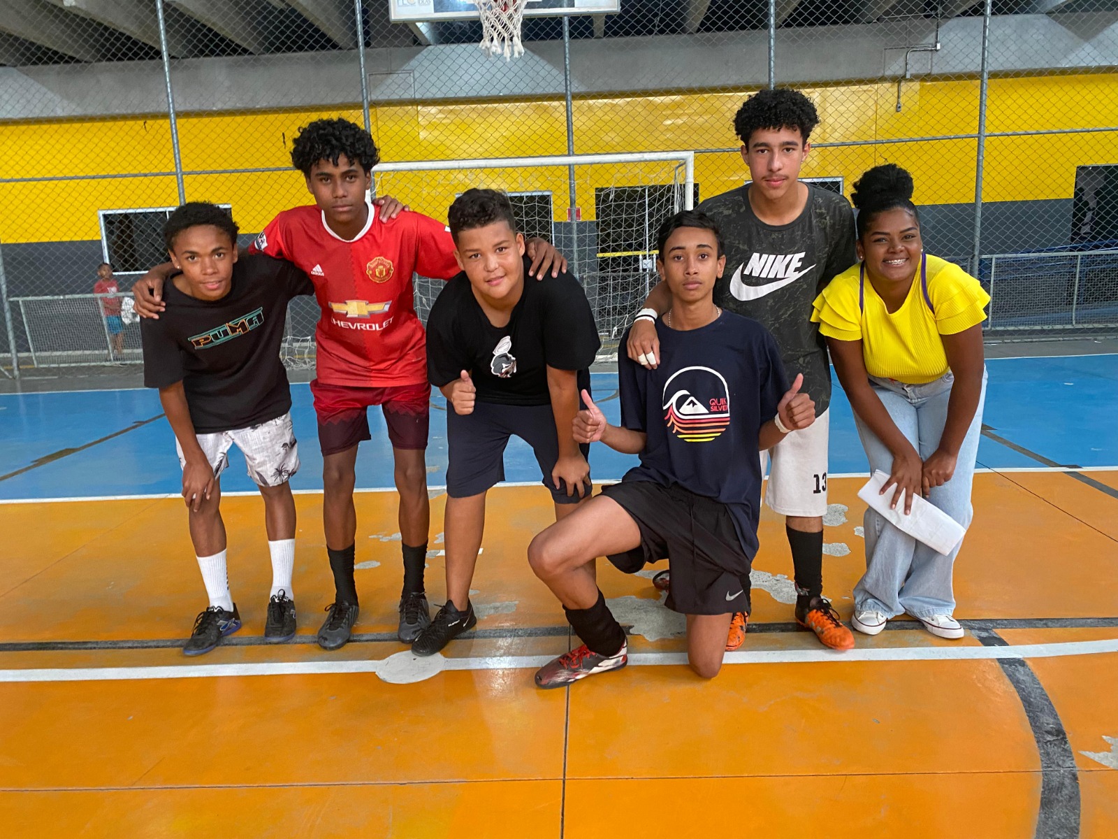 Cinco garotos e uma garota estão abraçados como na formação de um time de futebol para uma foto