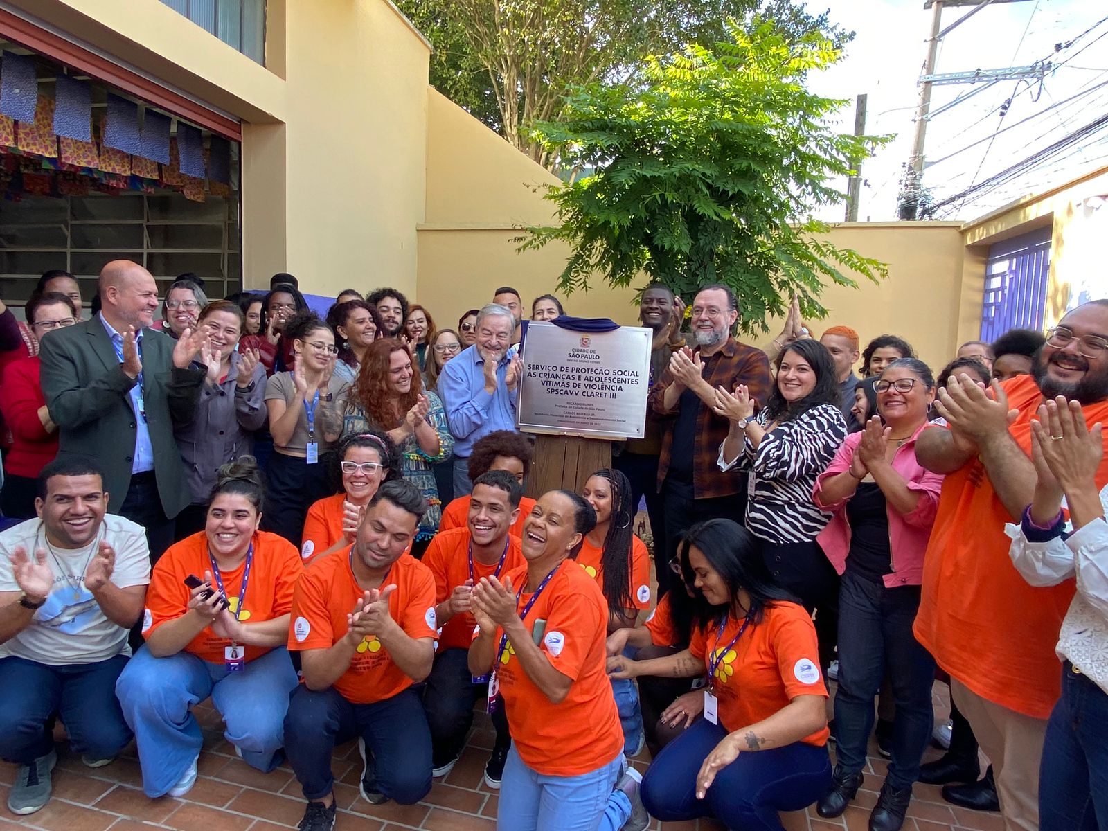 Pessoas reunidas aplaudem a inauguração. Na frente, pessoas vestem laranja como forma de representar o serviço. 