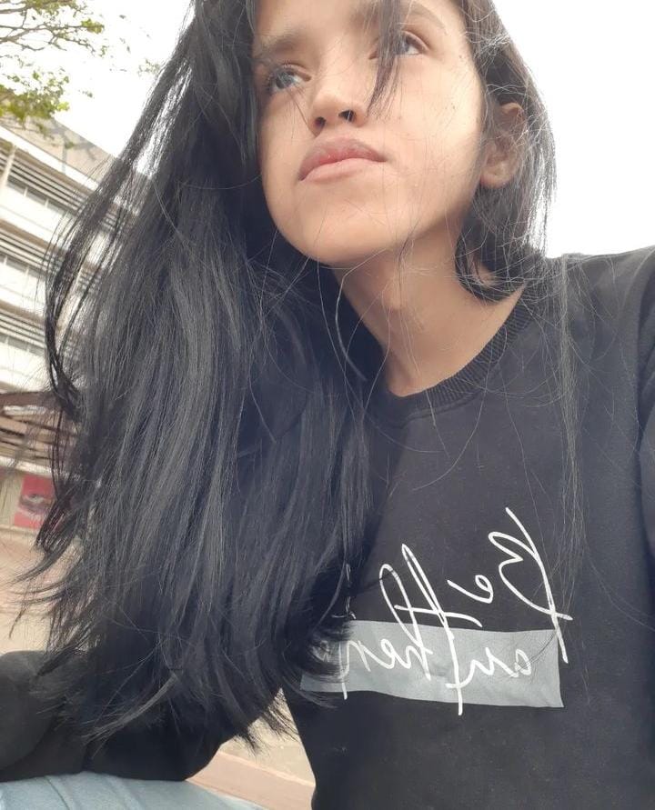 Com a câmera direcionada de baixo para cima, há uma mulher com seus cabelos longos e pretos enquanto olha para o horizonte. Ela está vestindo uma camisa preta de mangas longas.