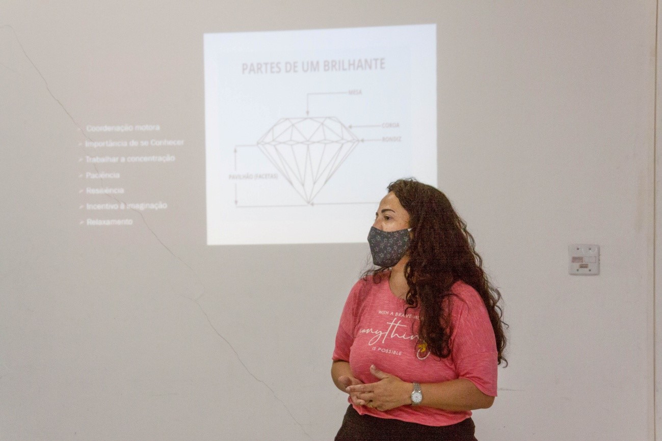 Imagem da palestrante diante de uma projeção na parede com a representação de um diamante.