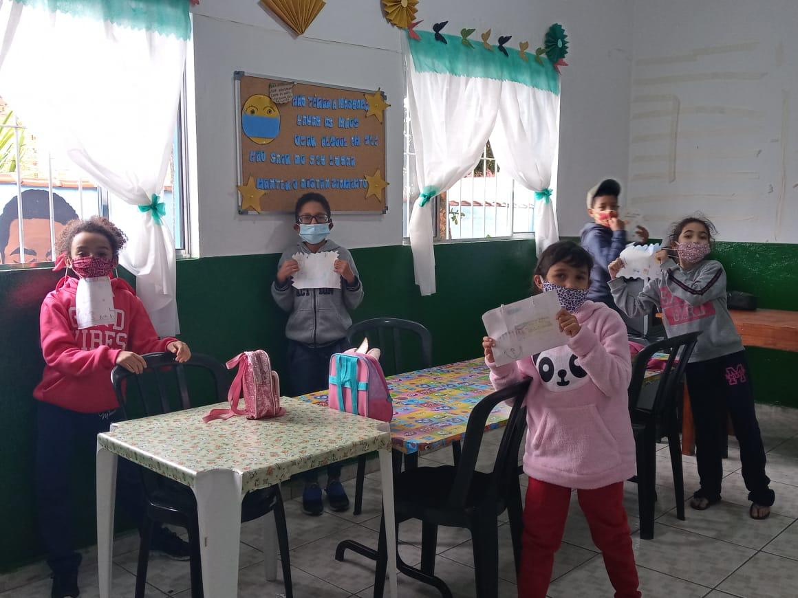Crianças mostrando seus desenhos feitos durante atividade da oficina de empoderamento social. Todos com máscaras e mantendo distanciamento. 