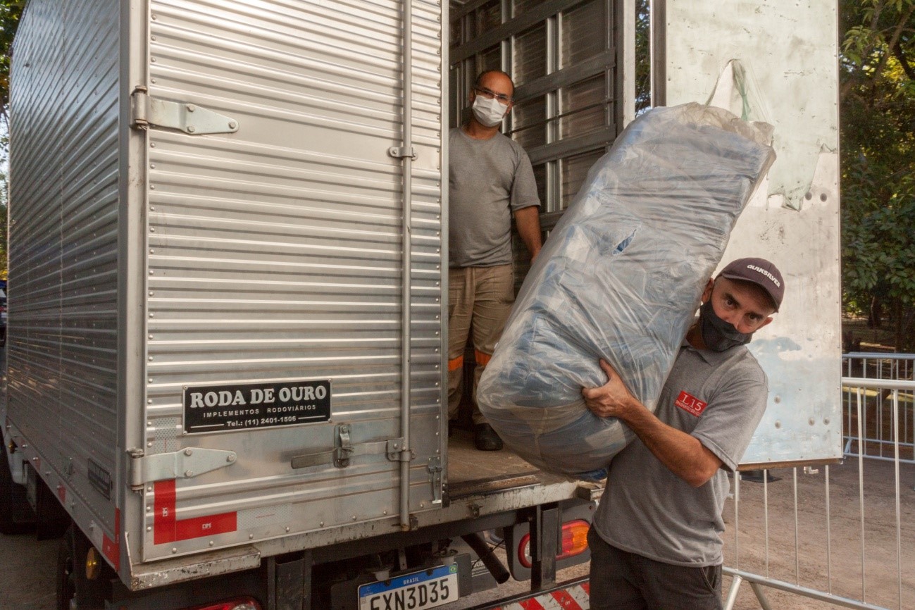 Dois homens descarregam o caminhão que levava os cobertores para serem entregues no Centro de Acolhimento Pelezão.