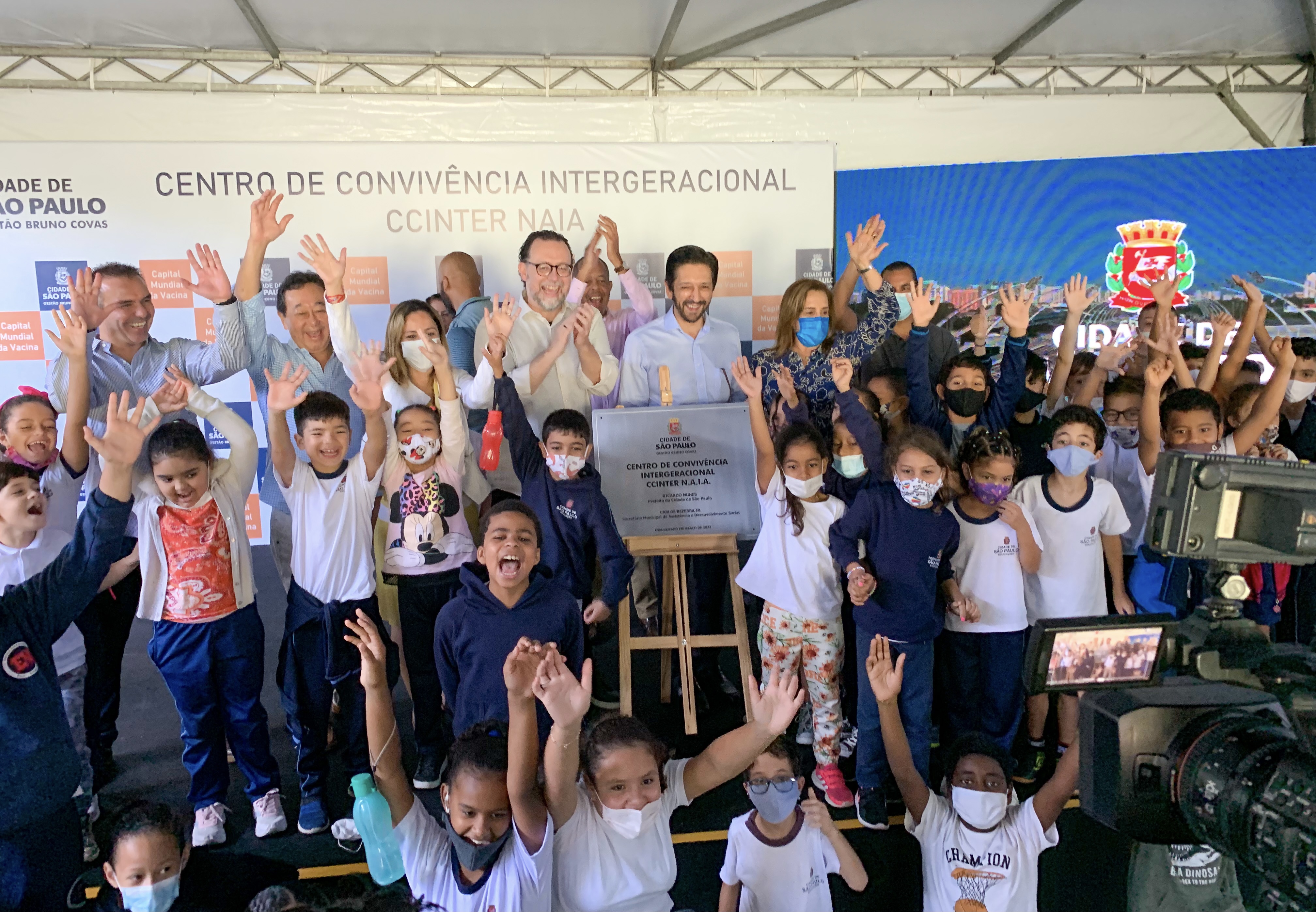 Secretario e Prefeito ao lado da placa de inauguração, rodeados de crianças com os braços para cima