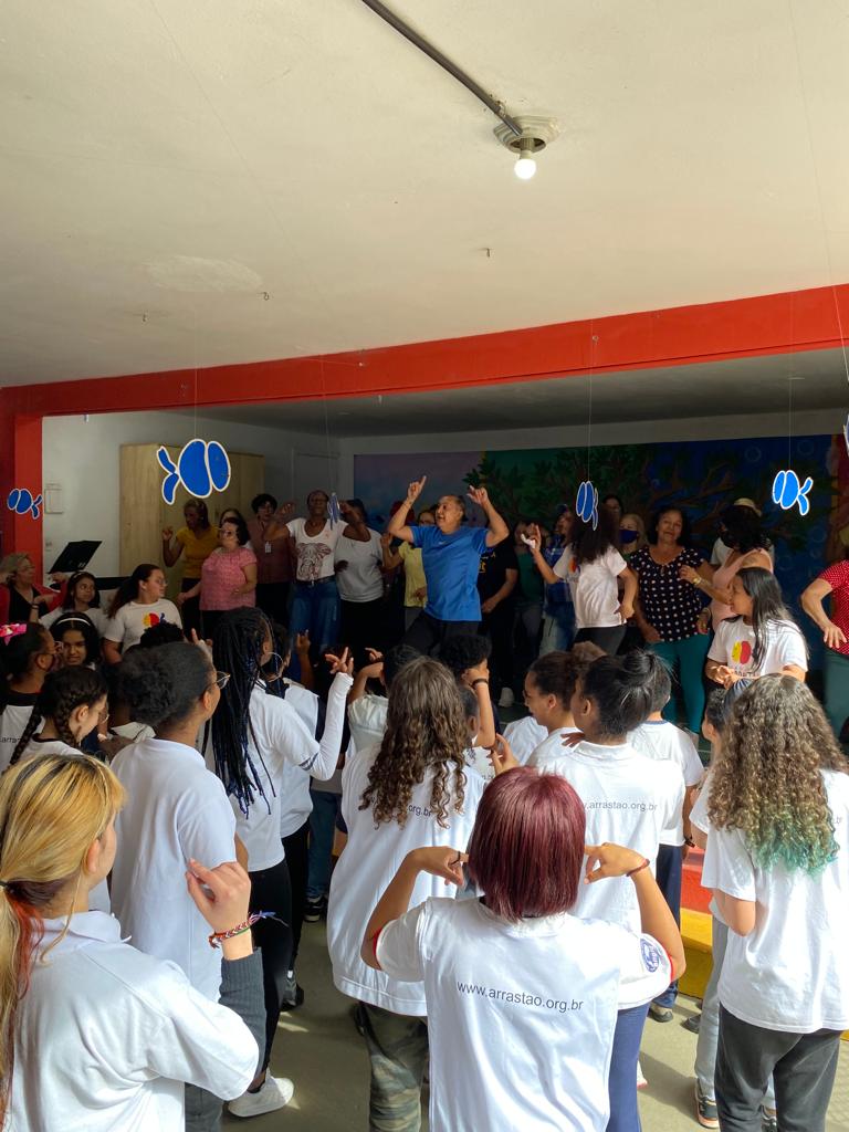 Idosos estão dançando no palco, e crianças estão observando a velha guarda e repetindo os passos. 