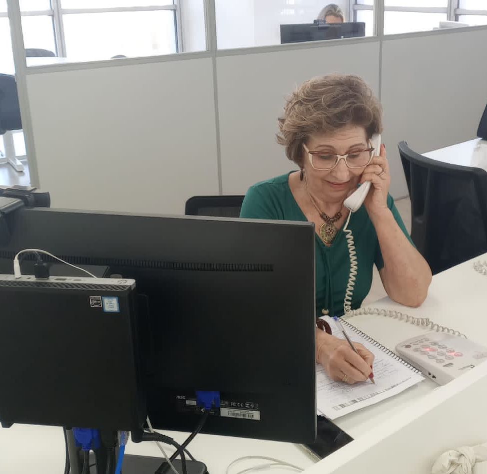 Uma mulher ao telefone, sentada em frente a uma tela de computador. 