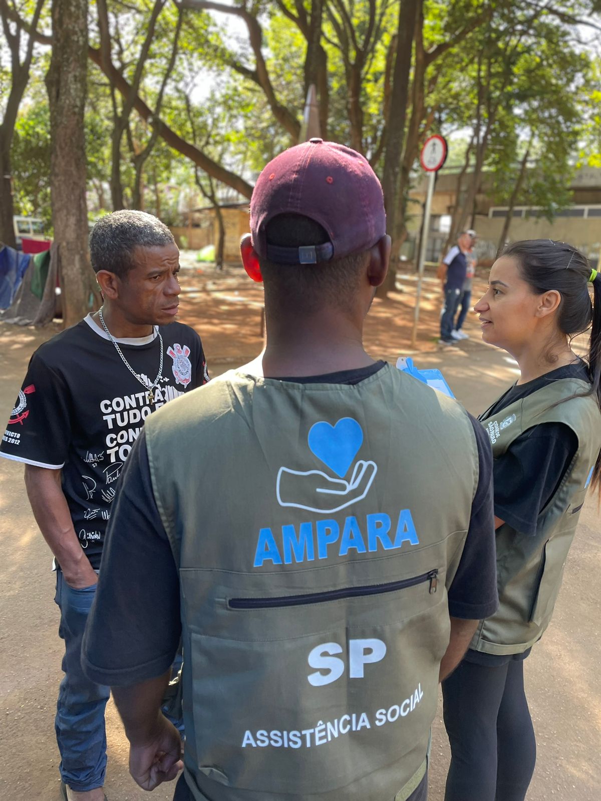 Três pessoas, sendo profissionais do Ampara SP e uma pessoa em situação de rua durante atendimento social.