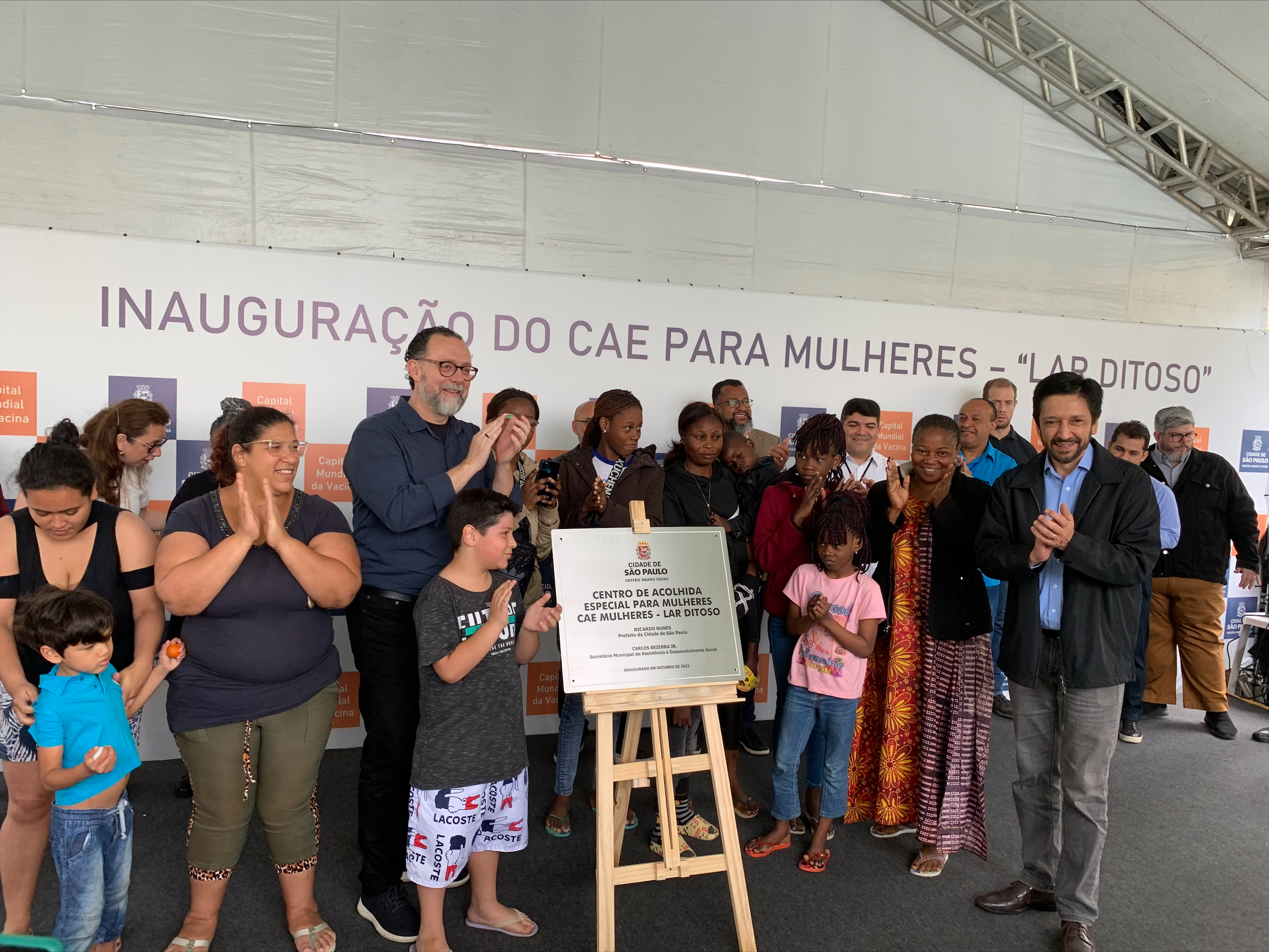 Secretário Carlos Bezerra Jr., Prefeito Ricardo Nunes e mais 17 pessoas no momento de descerramento da placa de inauguração do serviço. 