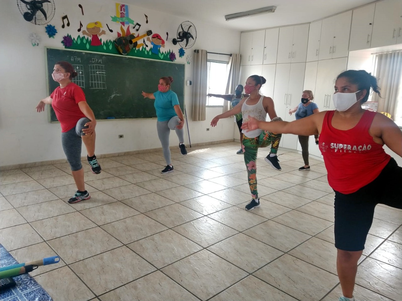 Seis mulheres de máscara praticando exercícios físicos.