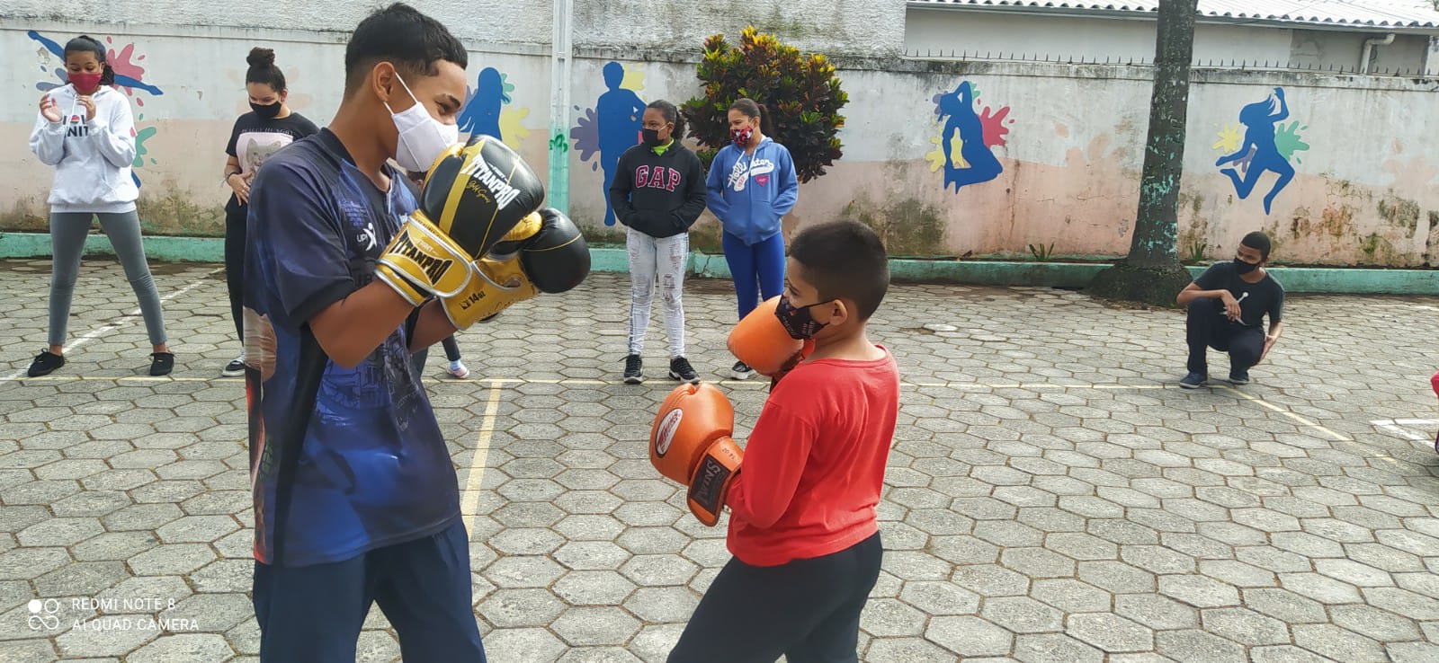 Foto com sete aluno de máscara, cinco dispostas ao fundo e duas a frente. Os dois meninos que estão na frente usam luvas de luta.