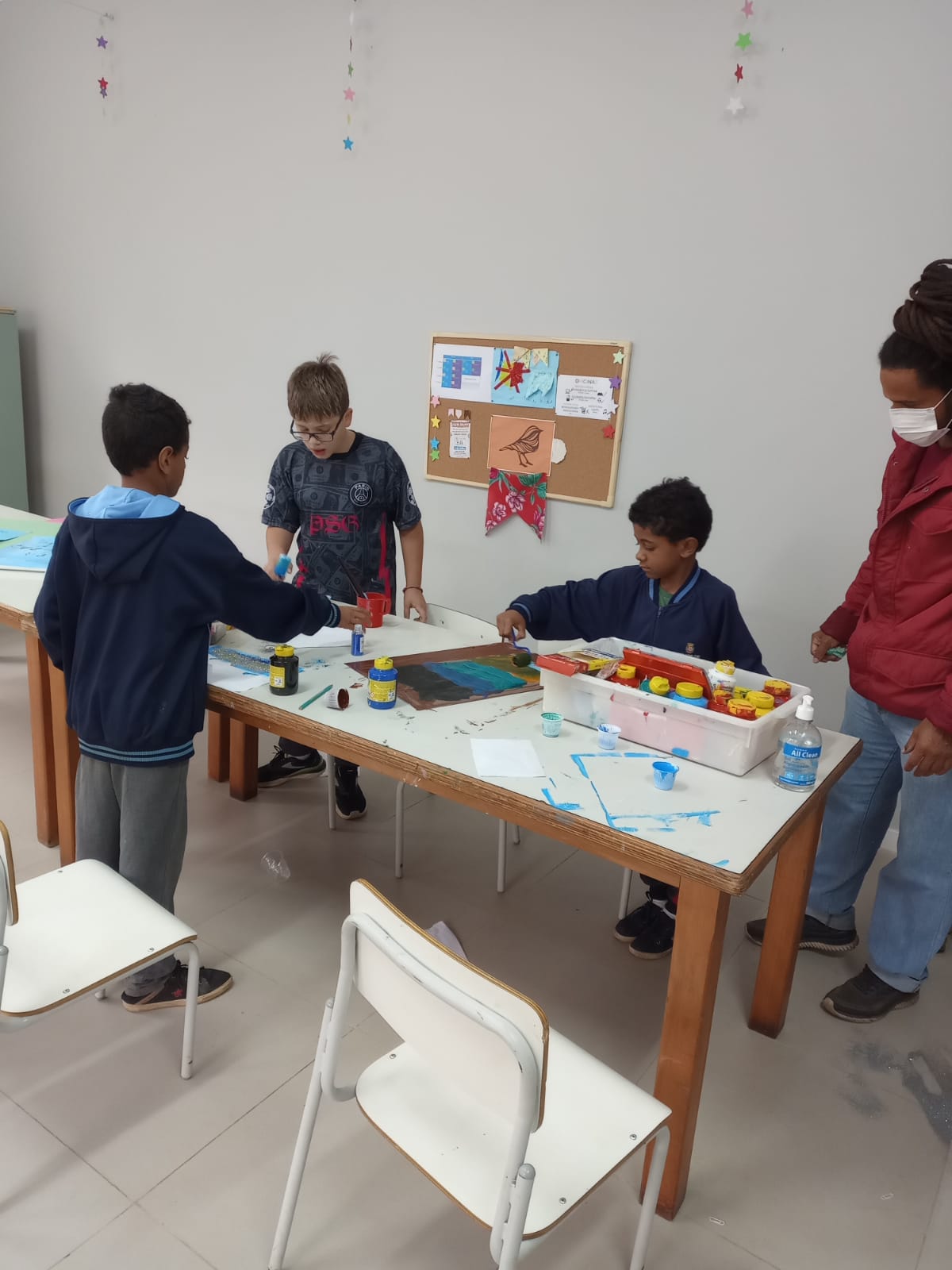 três meninos com idades entre 6 e 8 anos, pintando uma cartolina sobre uma mesa