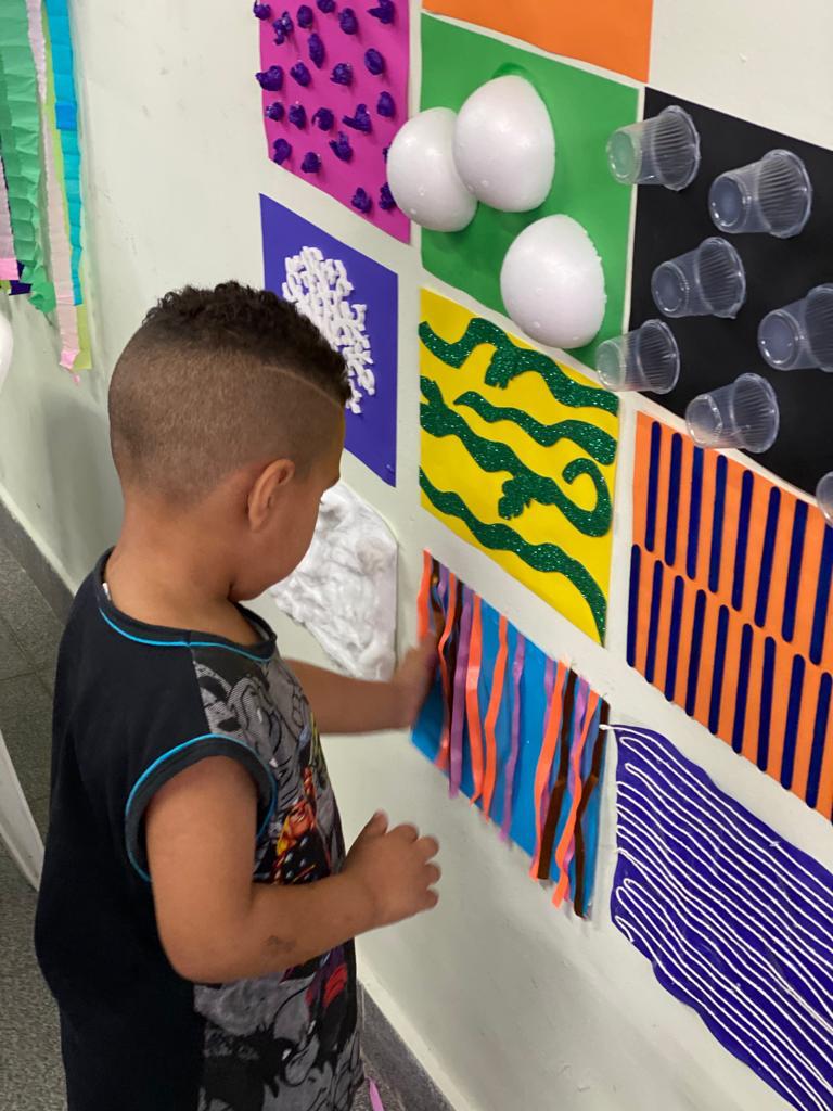 Foto: criança tocando no mural sensorial feito na parede do serviço.