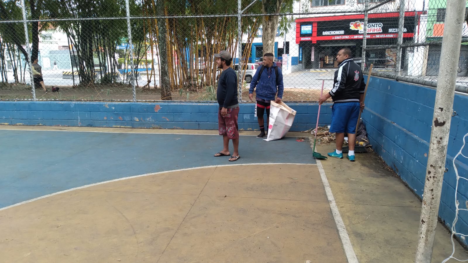 Acolhidos recolhem folhas que se acumularam na quadra poliesportiva da quadra