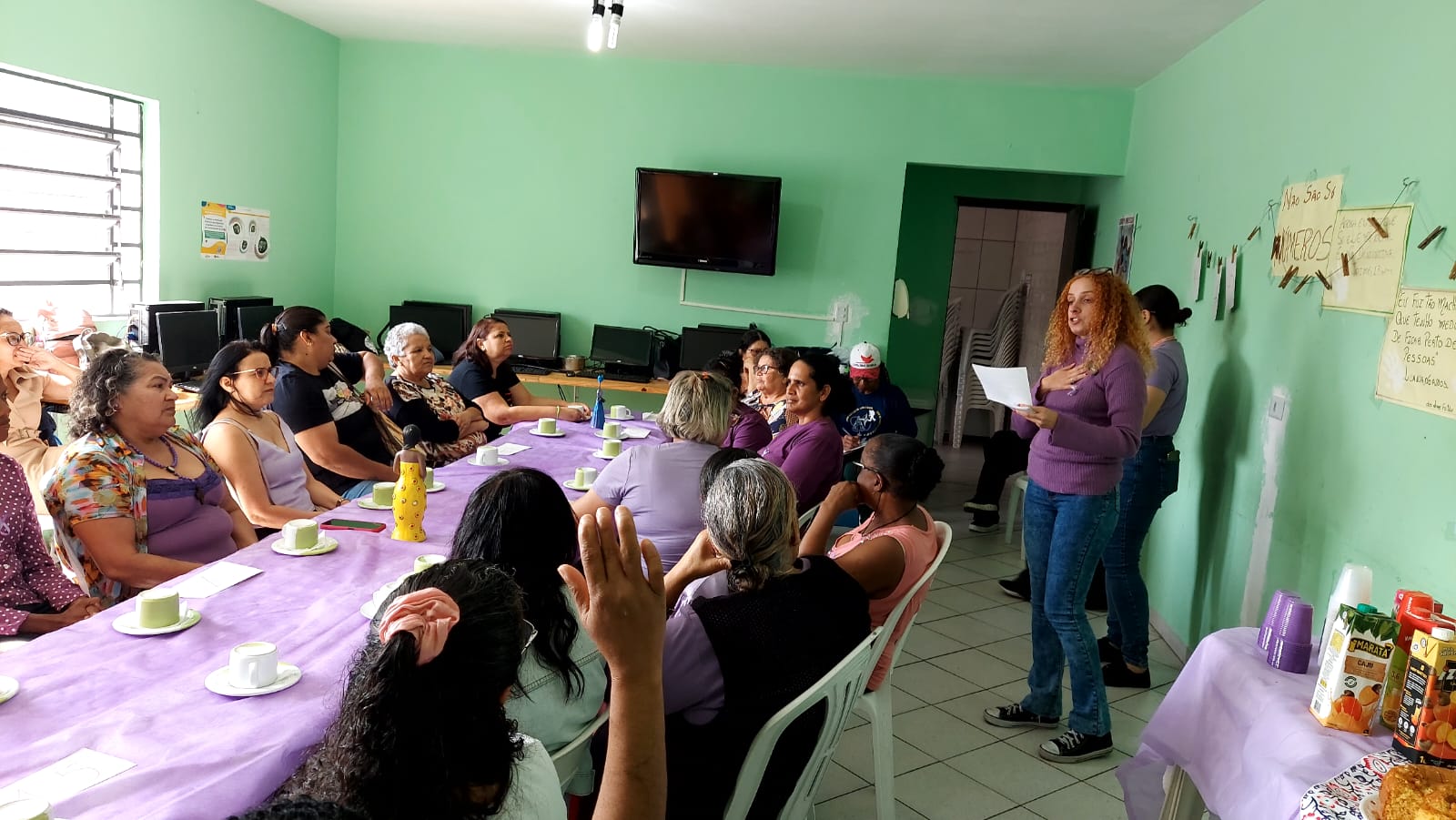 A maioria das mulheres estão sentadas aguardando o início da roda de conversa. Uma psicóloga do serviço, vestida de suéter roxo, está de pé lendo algum texto em uma folha sulfite.