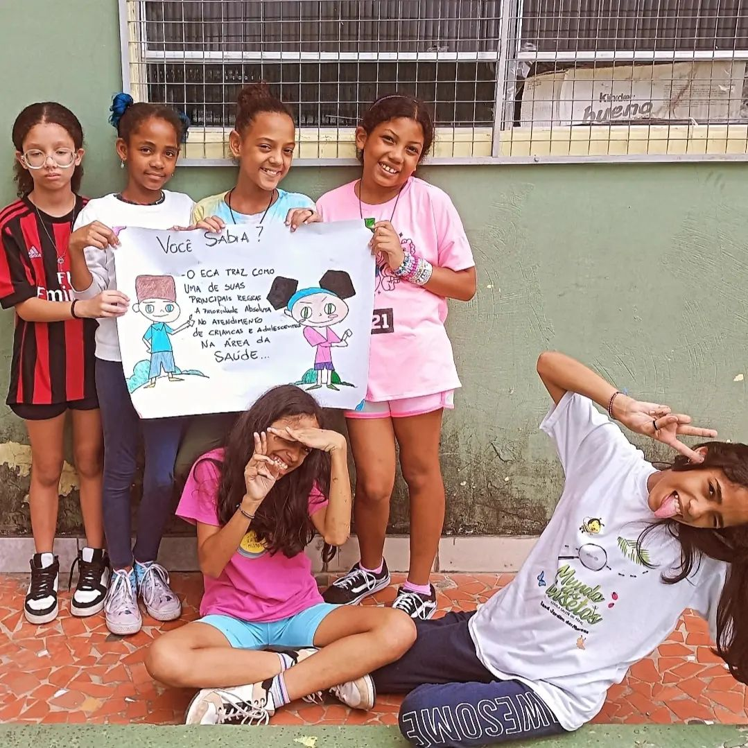 Meninas seguram cartaz sobre o atendimento prioritário na área da saúde