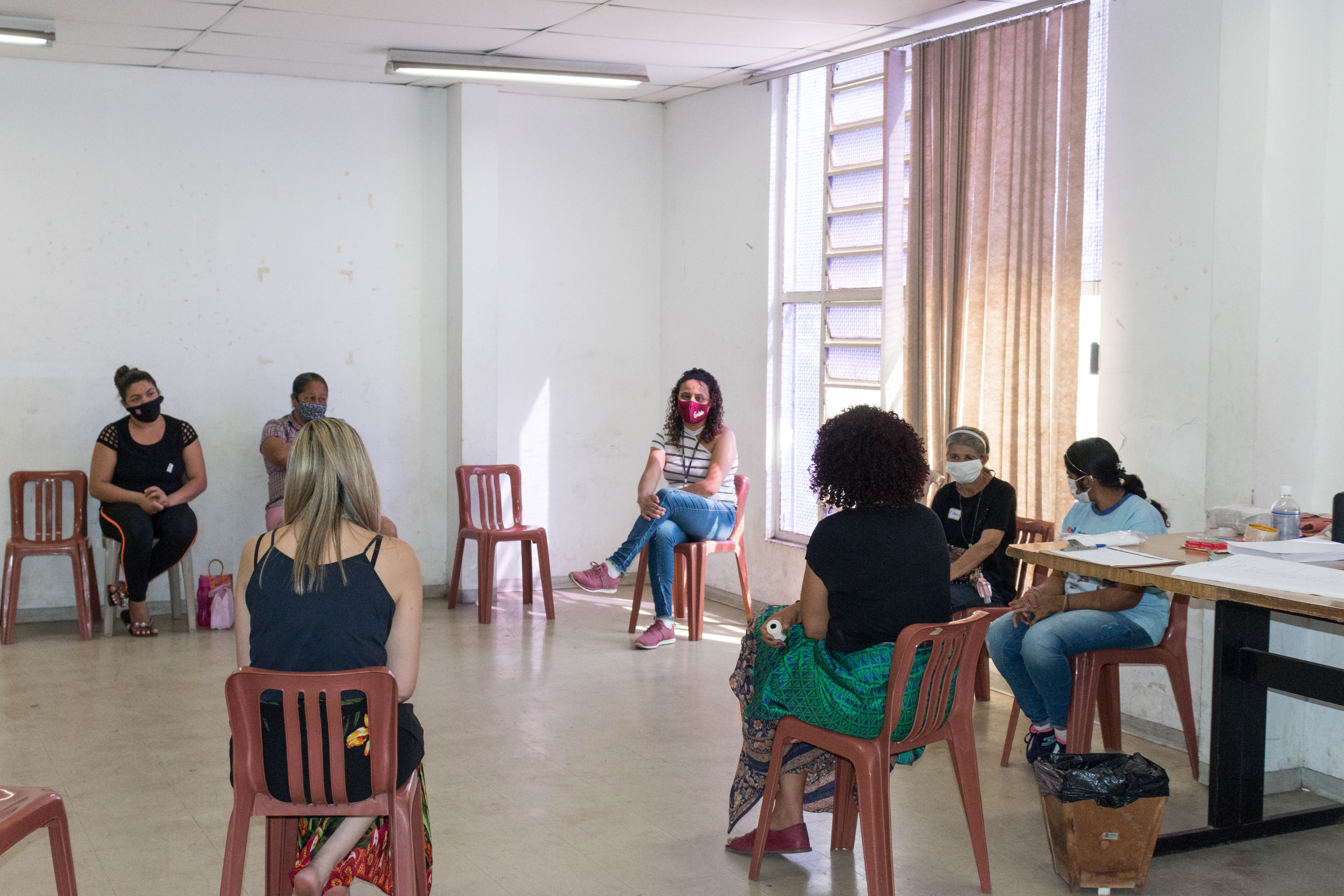 Foto da sala em que aconteceu o encontro com as mulheres adultas. As cadeiras estão dispostas em círculo e sete mulheres estão sentadas na roda