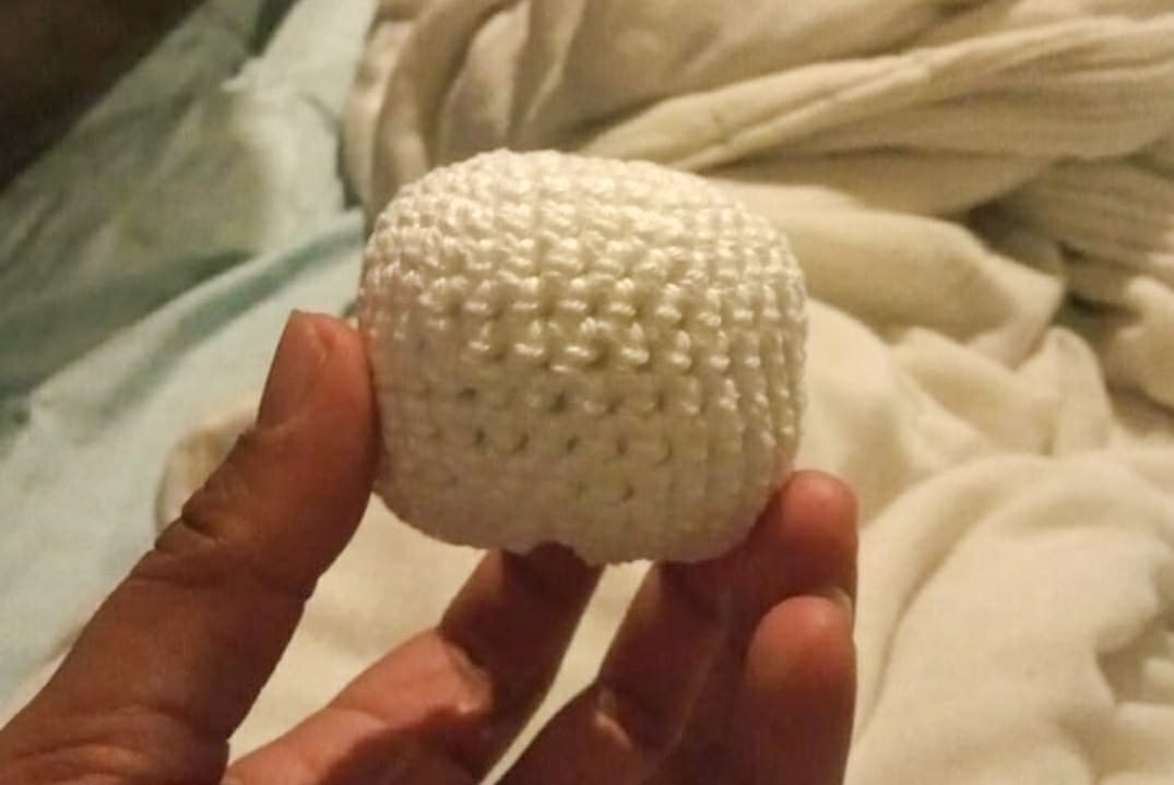 No centro da imagem está uma esfera confeccionada em lã branca segurada pela mão da pessoa que a fez