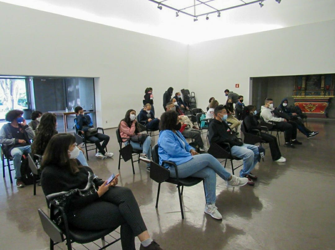 Foto da sala em que aconteceram as apresentações dos trabalhos com cerca de vinte pessoas sentadas em cadeiras seguindo o distanciamento social.