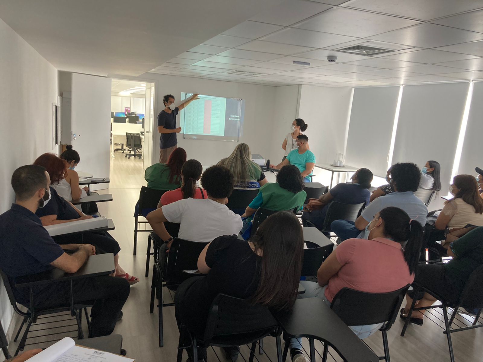 Homem em pé aponta para o slide ensinando os orientadores que estão sentados como deve ser feito o preenchimento na plataforma