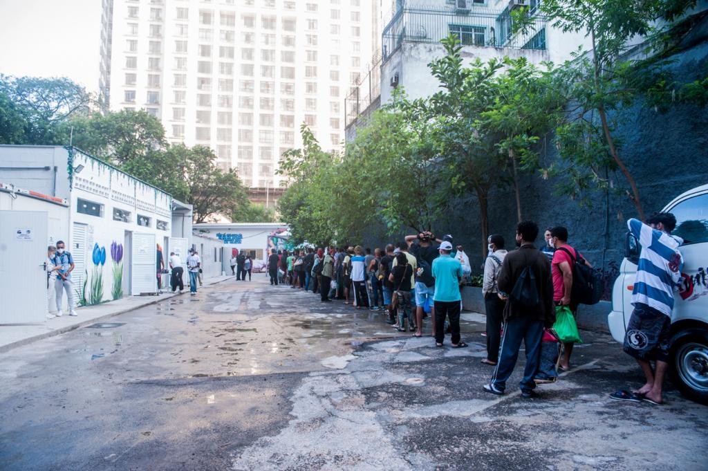 Pessoas enfileiradas na entrada do Núcleo aguardando liberação para acessarem o refeitório do local.
