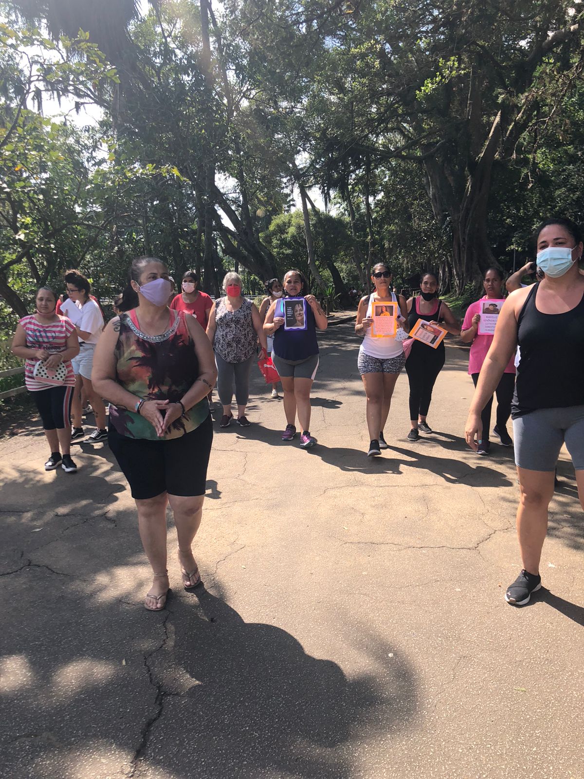 Imagem mostra mulheres caminhando no parque com cartazes em mãos, todas utilizando máscara.