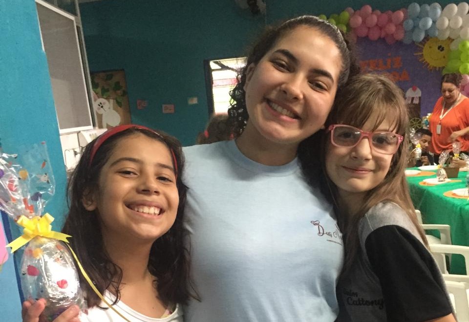Na imagem, a ex-atendida Anna Julia posa para a foto ao lado de duas adolescentes do CCA. Uma delas segura um ovo de chocolate.