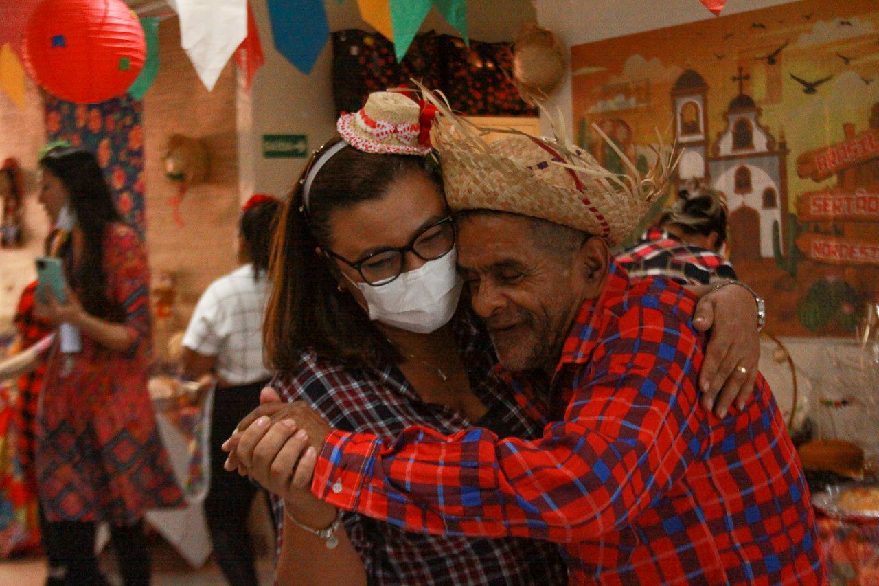 Na imagem aparece um homem e uma mulher dançando, utilizando roupas xadrez e chapéus de palha.