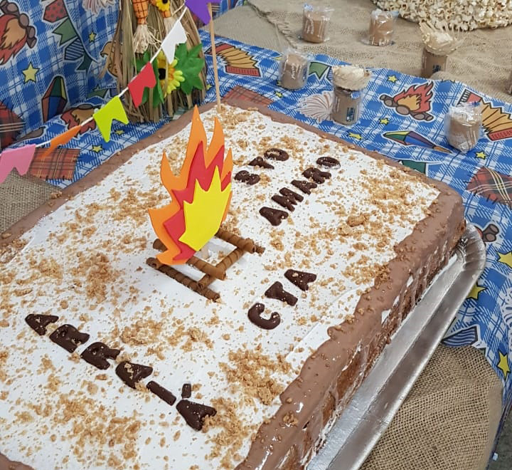 Bolo confeitado com os dizeres em cima, Arraiá CTA Santo Amaro, e uma labareda de fogo de papel enfeitando o bolo por cima