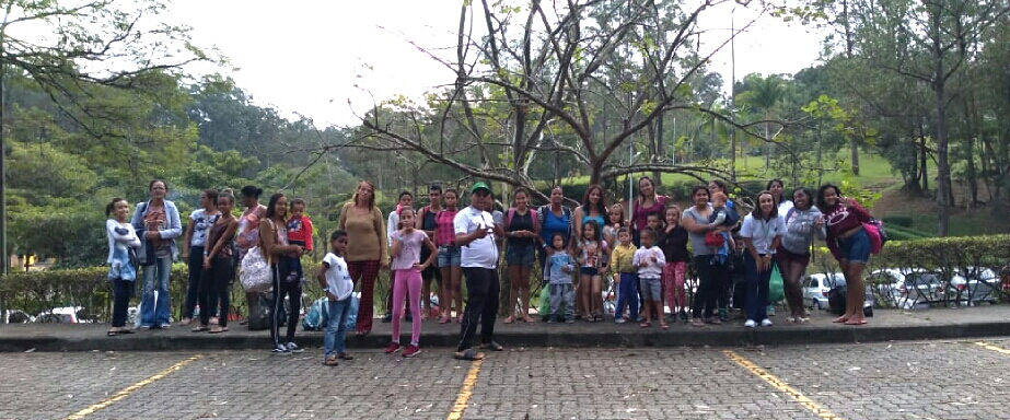 Pais, mães e filhos em pé no estacionamento do parque Ibirapuera com árvores ao fundo