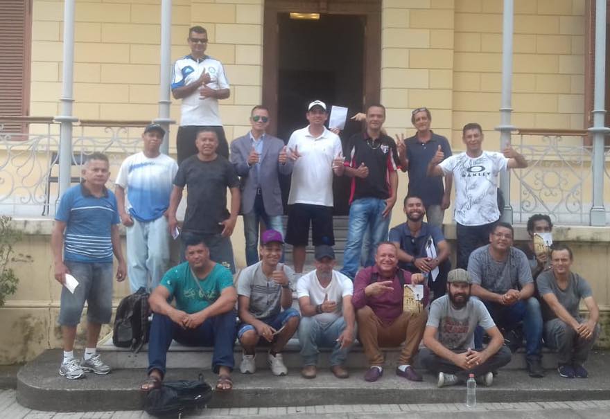 Usuários do serviço em frente ao museu com 9 sentados e 9 em pé