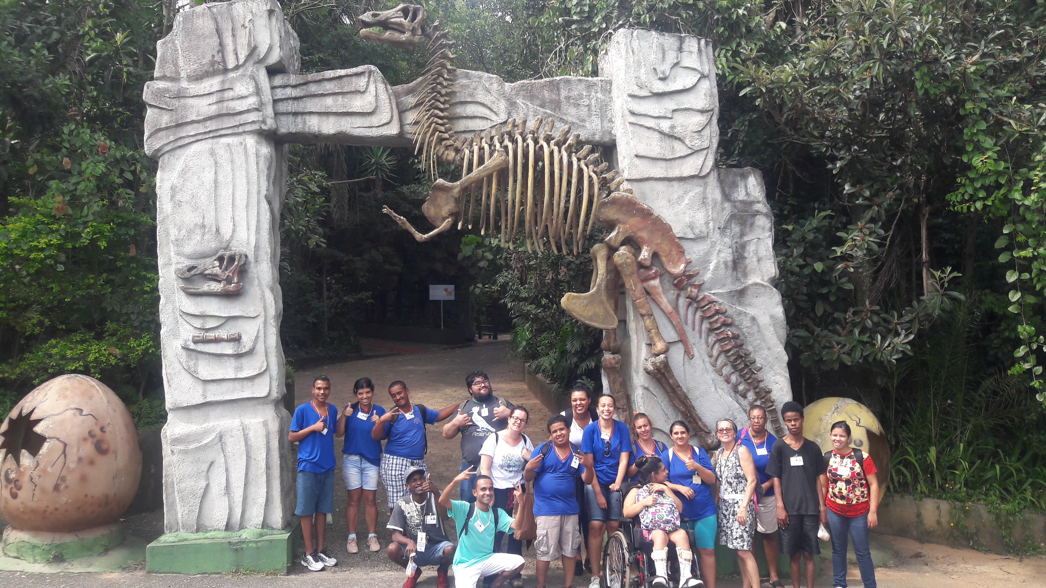 Dezessete conviventes e funcionários do serviço, sendo dez mulheres e sete homens, em frente à entrada do zoológico com réplica de dinossauro atrás