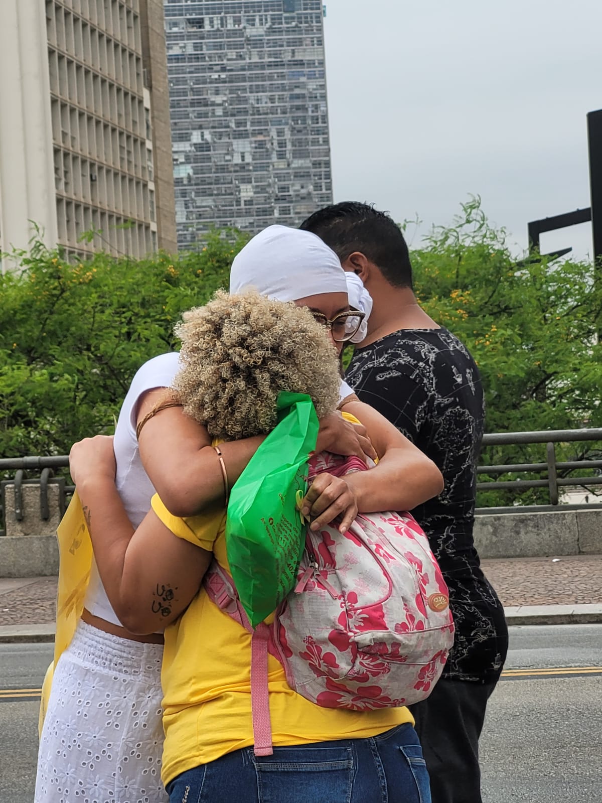 Na imagem mostra duas mulheres se abraçando, em meio aos prédios da cidade de São paulo. 