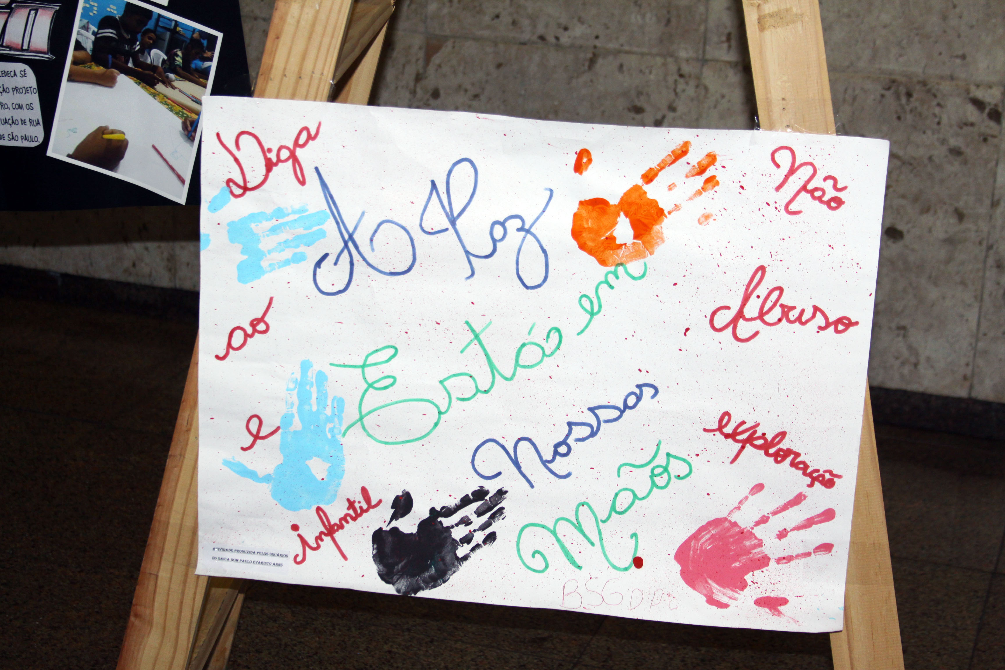 Cartaz feito por crianças e adolescentes, que está escrito "Diga não ao abuso e a exploração infantil" misturado com a frase "A paz está nossas mãos". Junto, há marcas de mãos pintadas com tinta.