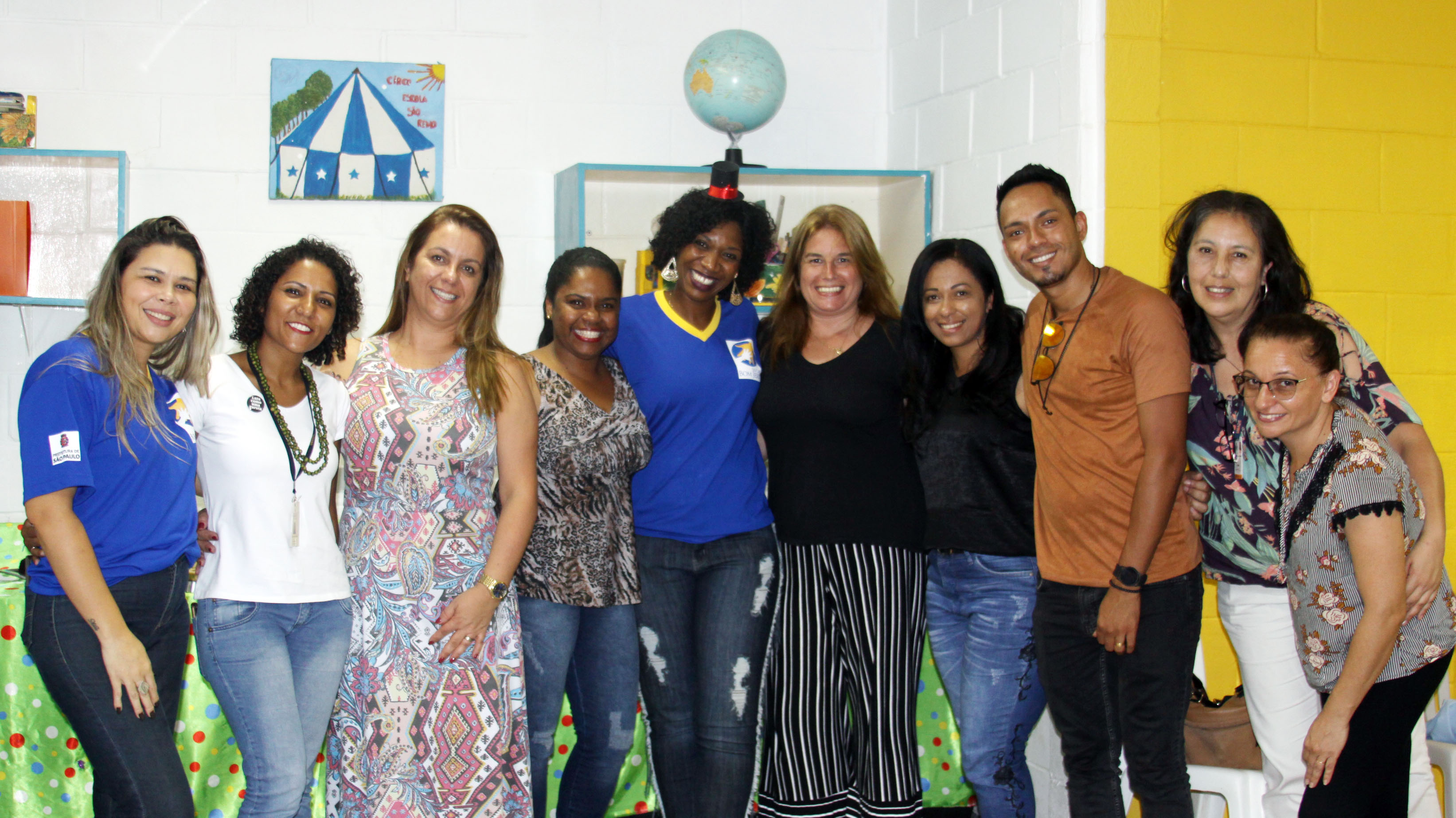 Dentro de uma sala do Circo Escola, gerentes, funcionários e coordenadores de projetos da ONG Social Bom Jesus posam para foto com a Gestora de Parcerias do CRAS Butantã e Supervisora da região