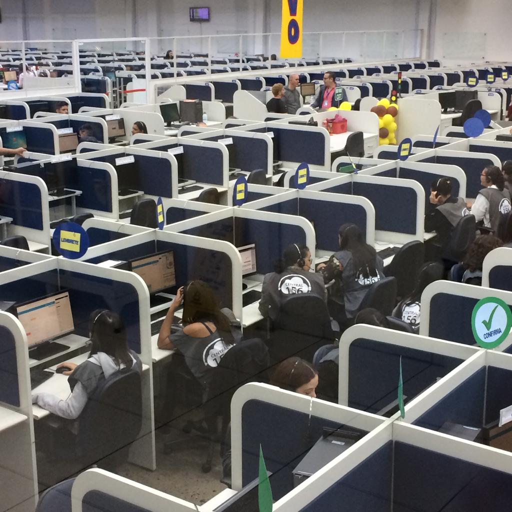 Operadores da Central São Paulo Um Cinco Meia atendendo munícipes ao telefone em sala com divisórias individuais brancas e azuis