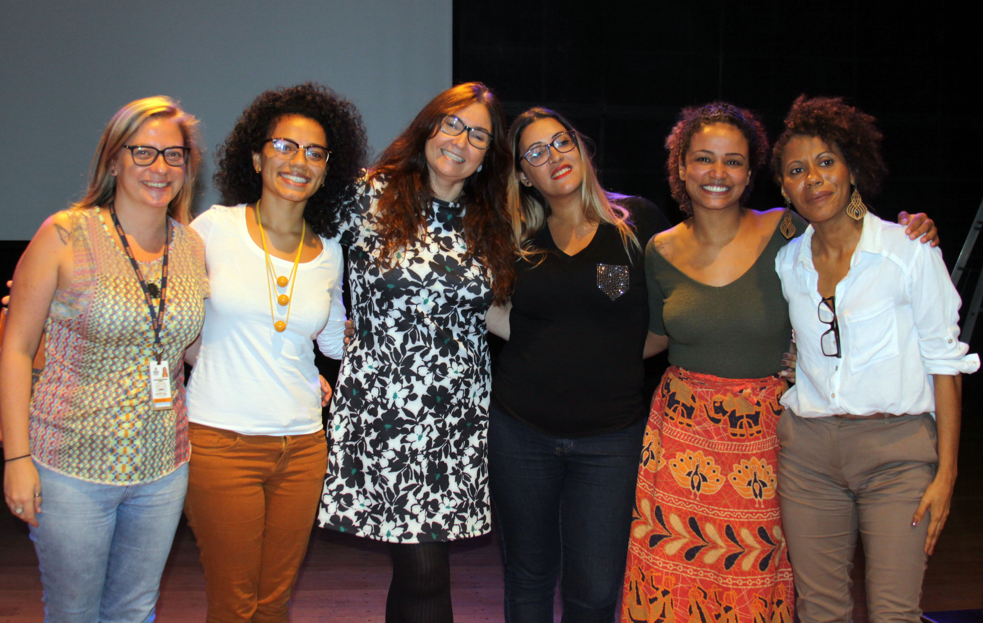 Posam para a foto, no palco do auditório, mulheres palestrantes e organizadoras do evento.